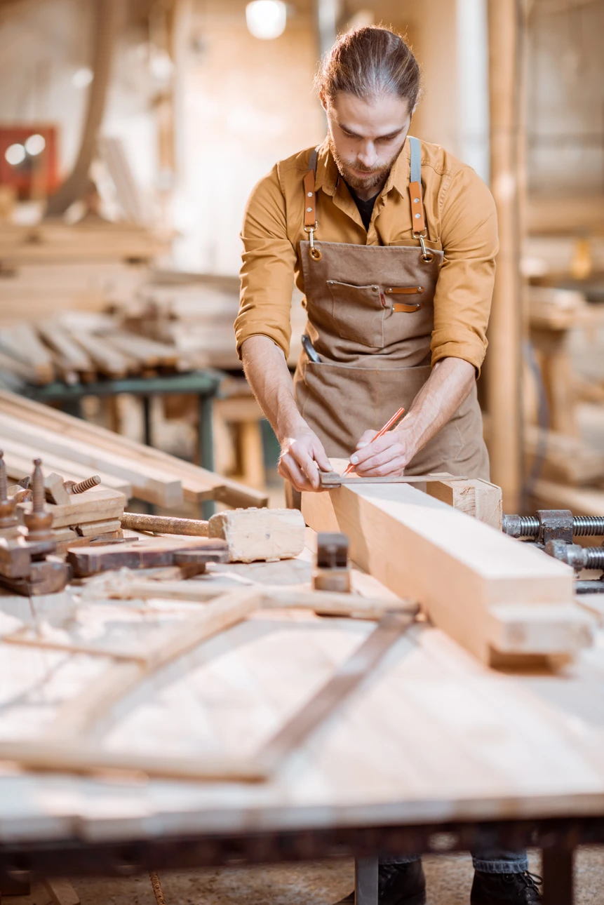 Artisan menuisier travaillant le bois dans son atelier, utilisant un rabot manuel sur une planche posée sur établi